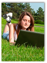 Young woman lying in grass working on her laptop.