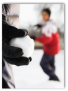 Close up shot of a gloved hand holding a snowball and a blurred person in background getting ready to throw a snowball