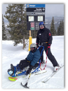 Photo of Cynthia Dietrich on a sled with hand skiis at the top of a mountain with an assistant behind her