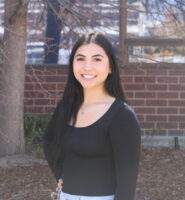 A woman with dark hair and a black top poses outside