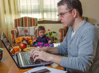 dad working on computer with child playing next to him