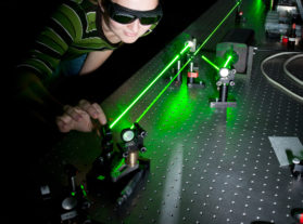 Woman working on optics equipment with green lasers.