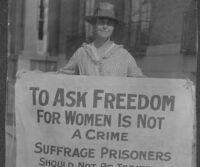 black and white photo of woman holding a sign that says "To ask freedom for women is not a crime. Suffrage prisoners should not be treated as criminals."