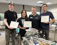 Three students holding diplomas with the Dean