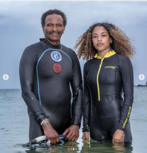 Kamau Sadiki and Jewell Humphrey in wetsuits standing in the ocean (National Geographic, March 2022)
