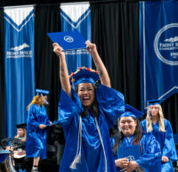 Smiling FRCC graduate in blue cap and gown holding up her diploma