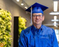 Jim smiling wearing his blue cap and gown