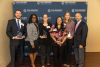 A group poses in front of a blue backdrop while holding awards.