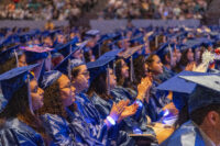 Seated graduates in blue caps and gowns clapping