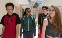 Four smiling students walking down an FRCC hallway together