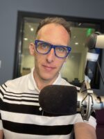 Colorado Public Radio host Ryan Warner in front of a large microphone in a recording studio.