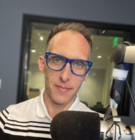 Colorado Public Radio host Ryan Warner in front of a large microphone in a recording studio.