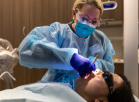 Student in surgical gown and purple gloves working on a patient in the dental chair at the clinic