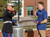 Ethan holding a folded flag while saluting a fellow solider in uniform